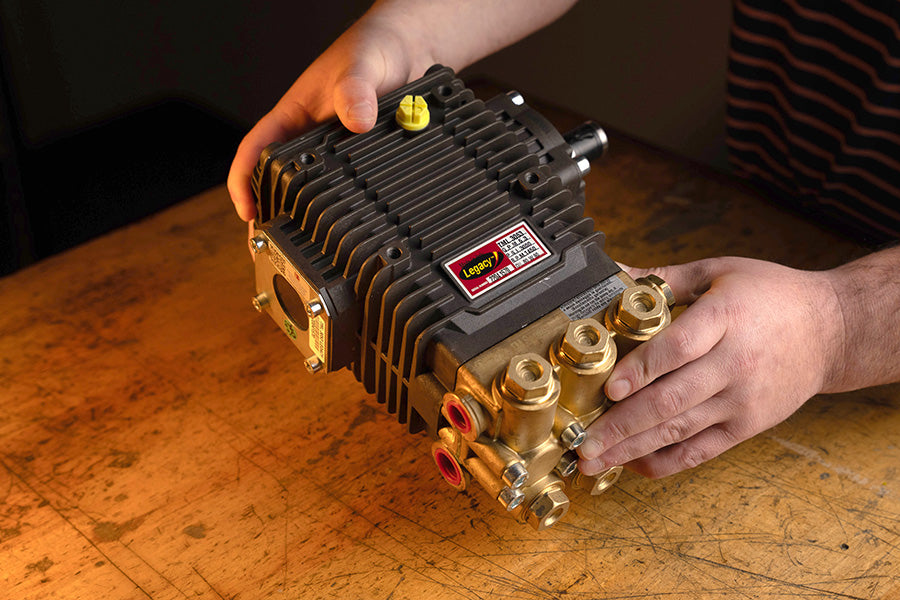 Person holding a pressure washer pump on a wooden workbench
